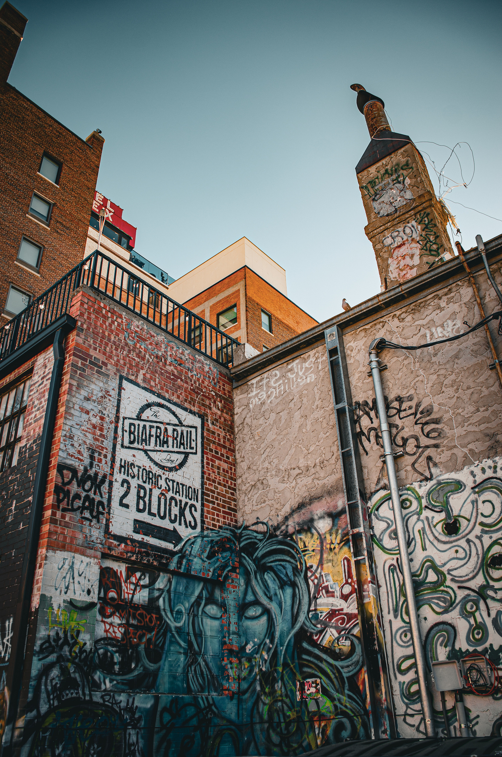 Street art emerges from textured walls in a symphony of color and form. A monumental face peers out from layers of graffiti, creating a dialogue between artistic styles.