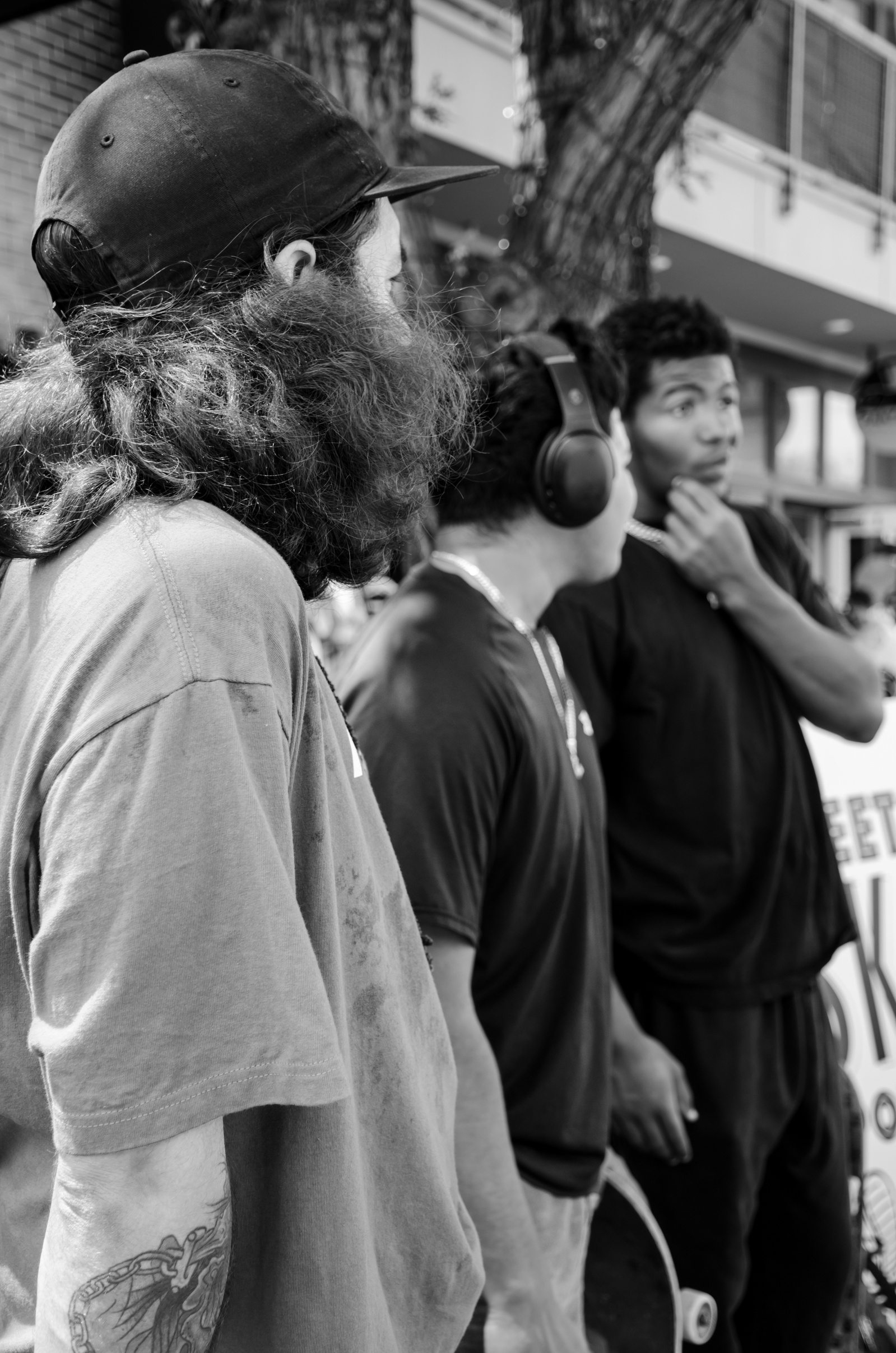 Three figures in profile, caught mid-thought. One wears headphones like armor, another watches the world with a guarded jaw. Their bodies lean just forward, always forward—into the noise, into the blur.