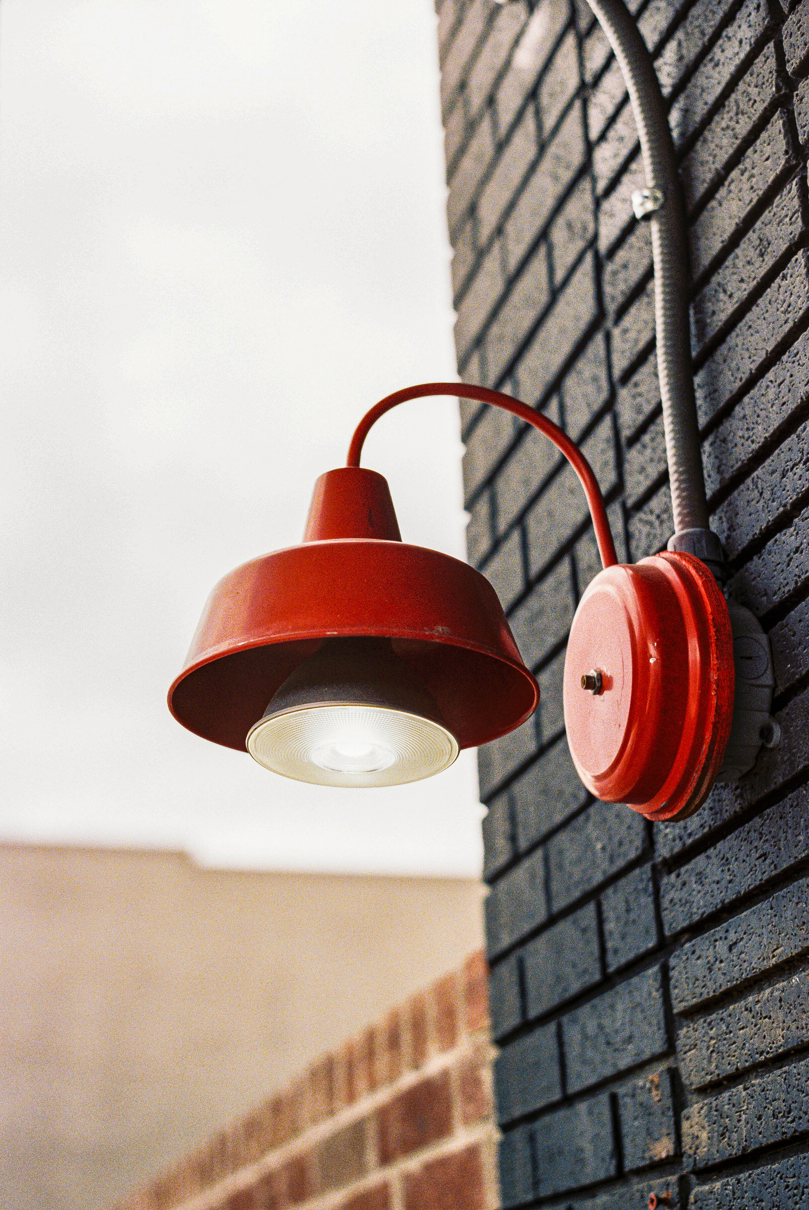 An old-school wall lamp burns gently against dark bricks, holding its own kind of ceremony at dusk. It’s a simple ode to light, texture, and the timelessness of design.