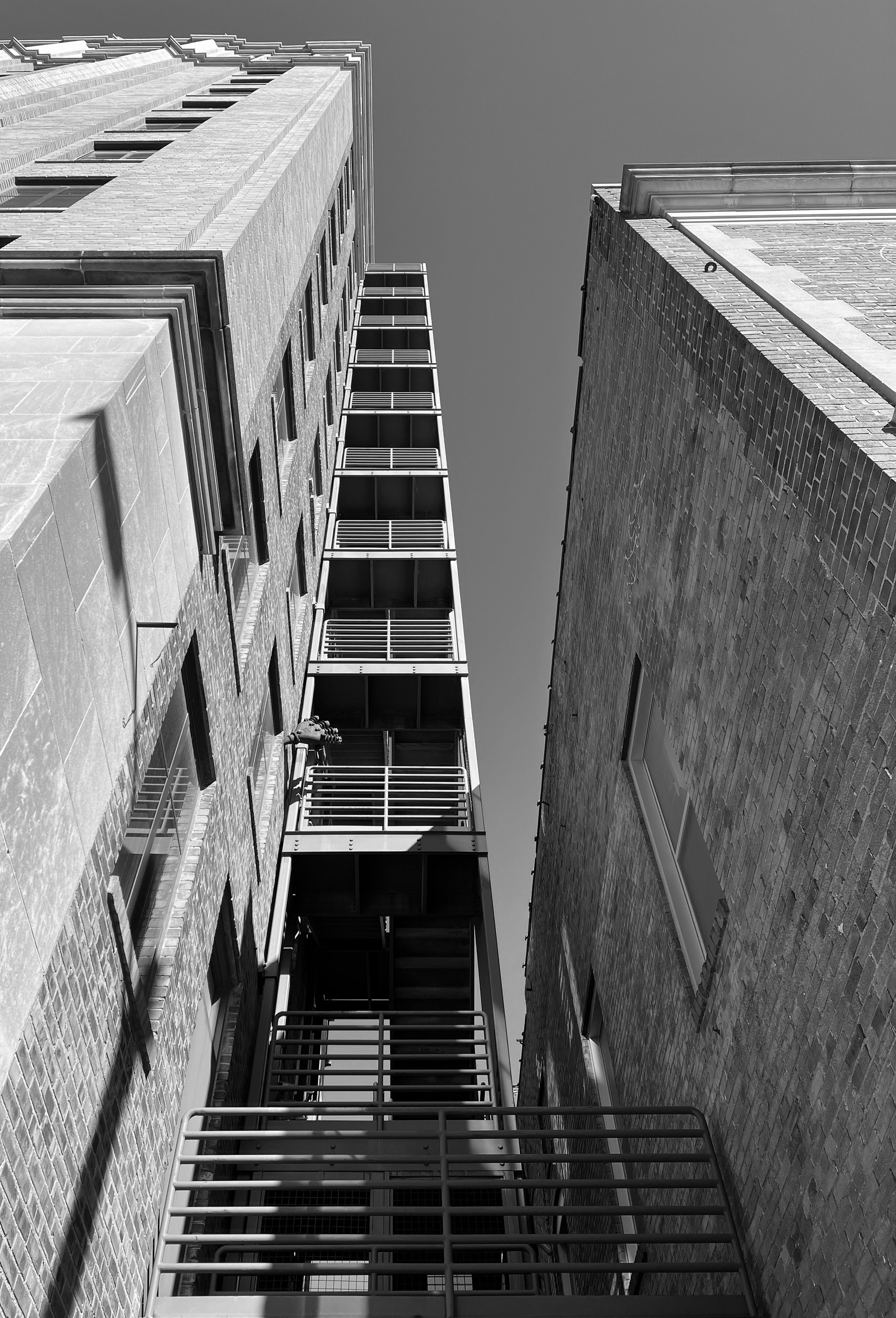 Two brick walls and a sliver of sky. In the compression, silence becomes something physical. The staircase rises like a thought you can’t let go of. Hard light. Harder questions.