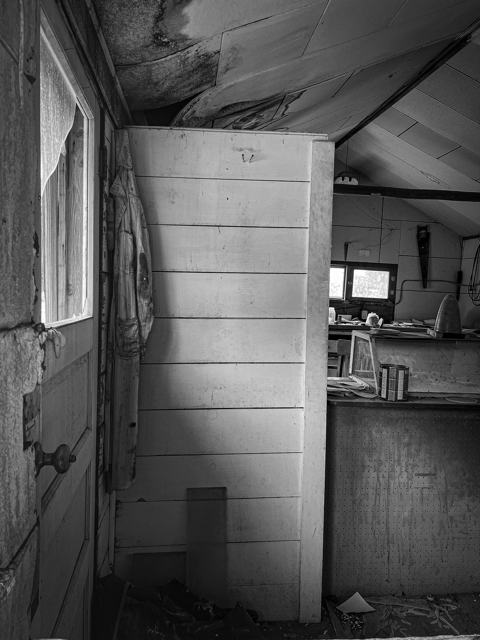 A coat still hangs, casting its silhouette like memory against the cracked ceiling. It's as if someone stepped out mid-task and forgot to return, leaving the moment open-ended.