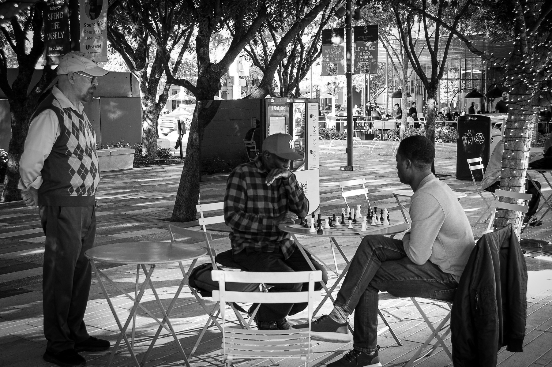 Every move is a study in restraint. Beneath the trees, strategy replaces speech and time loosens its grip. A sidewalk tournament becomes something ancient—ritual, rivalry, and respect in public view.