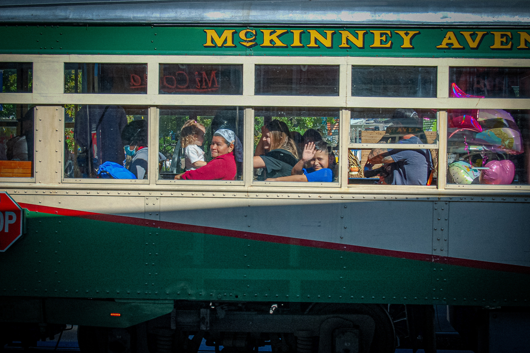 A vintage trolley holds stories behind each window pane. Laughter, weariness, and curiosity travel side by side, as a boy waves outward—an echo of childhood wonder within the city's steady pulse.
