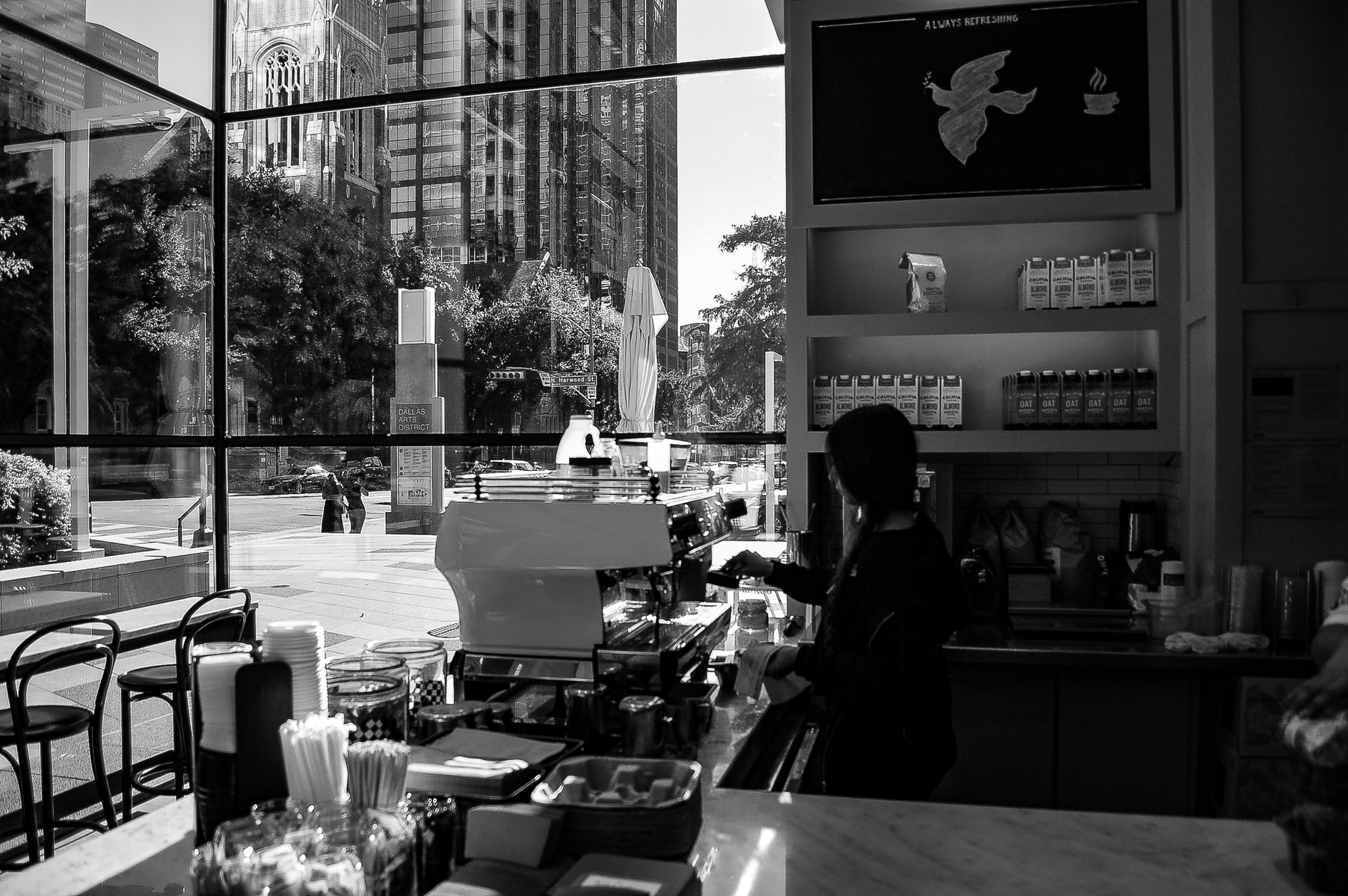 A quiet transaction layered against the hum of the city—this moment folds two worlds into one: the interior rituals of routine and the reflective sprawl of the skyline beyond. Presence becomes reflection. Stillness becomes performance.