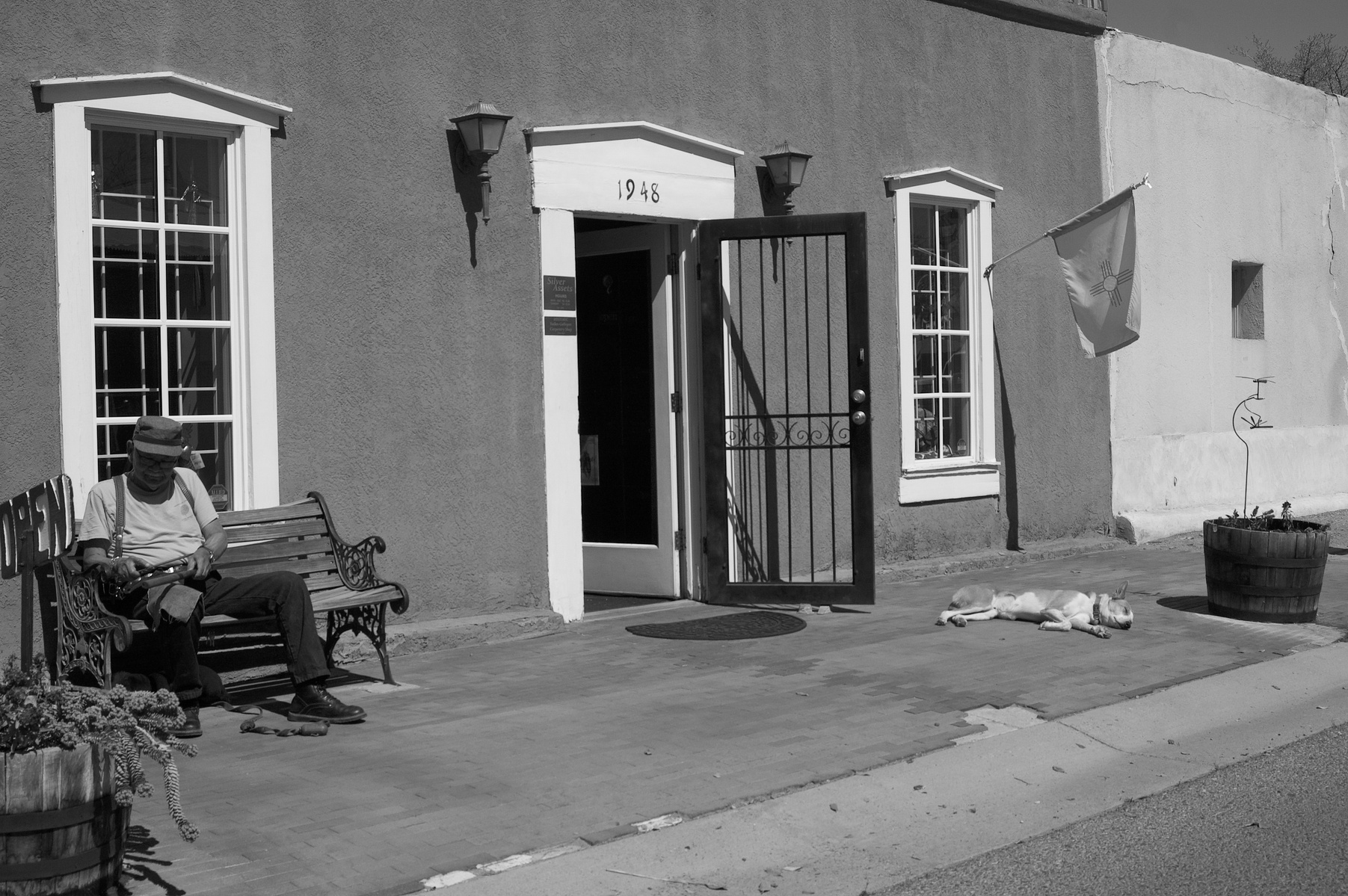 Warm bricks, open doors, and the weight of nothing to do. The man leans into the slow hour; the dog is already gone to dream. Life unfolds quietly where no one is rushing.