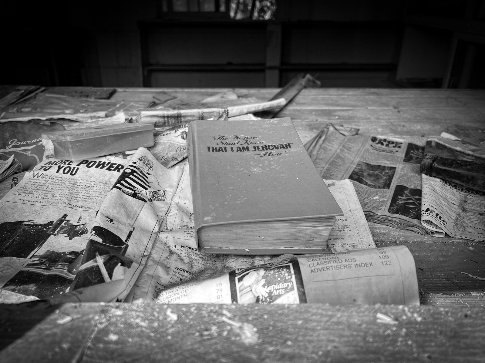 A book rests unopened, flanked by yellowing pages and static dust — frozen in mid-thought. The room around it has quieted, but the intent still breathes in the things left behind.