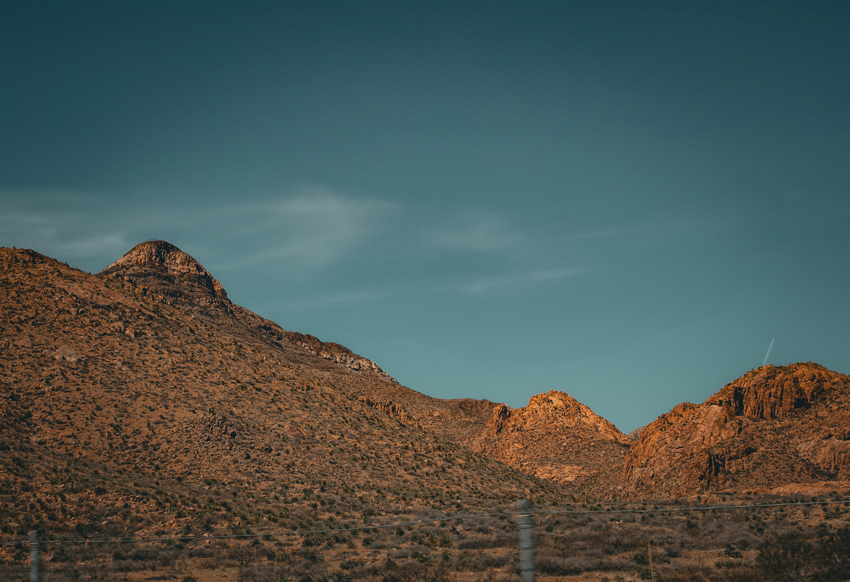 A lone formation leans into the last warmth of the day, its outline catching flame as if to mark a moment no one will name. The foreground slips past, blurred by movement—an echo of passage with no origin, no destination.