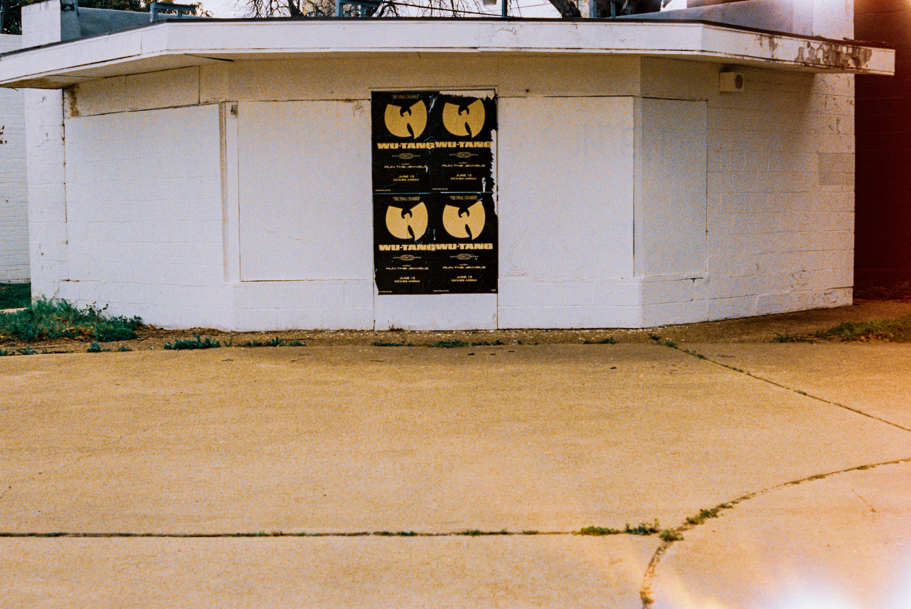An empty wall pulsing with quiet rebellion. The repeated Wu-Tang posters mark presence in absence, claiming space on a structure whose purpose has long since faded.