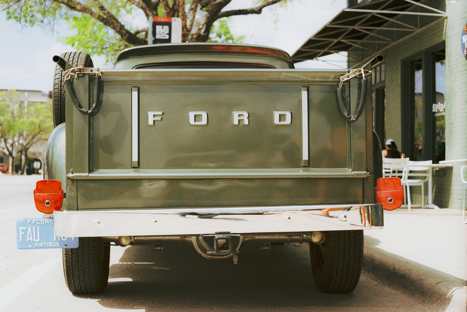 A vintage Ford truck glows under spring light, its deep green metal polished to mirror the street behind it. Clean lines, chrome gleam—this is pride in design, preserved.