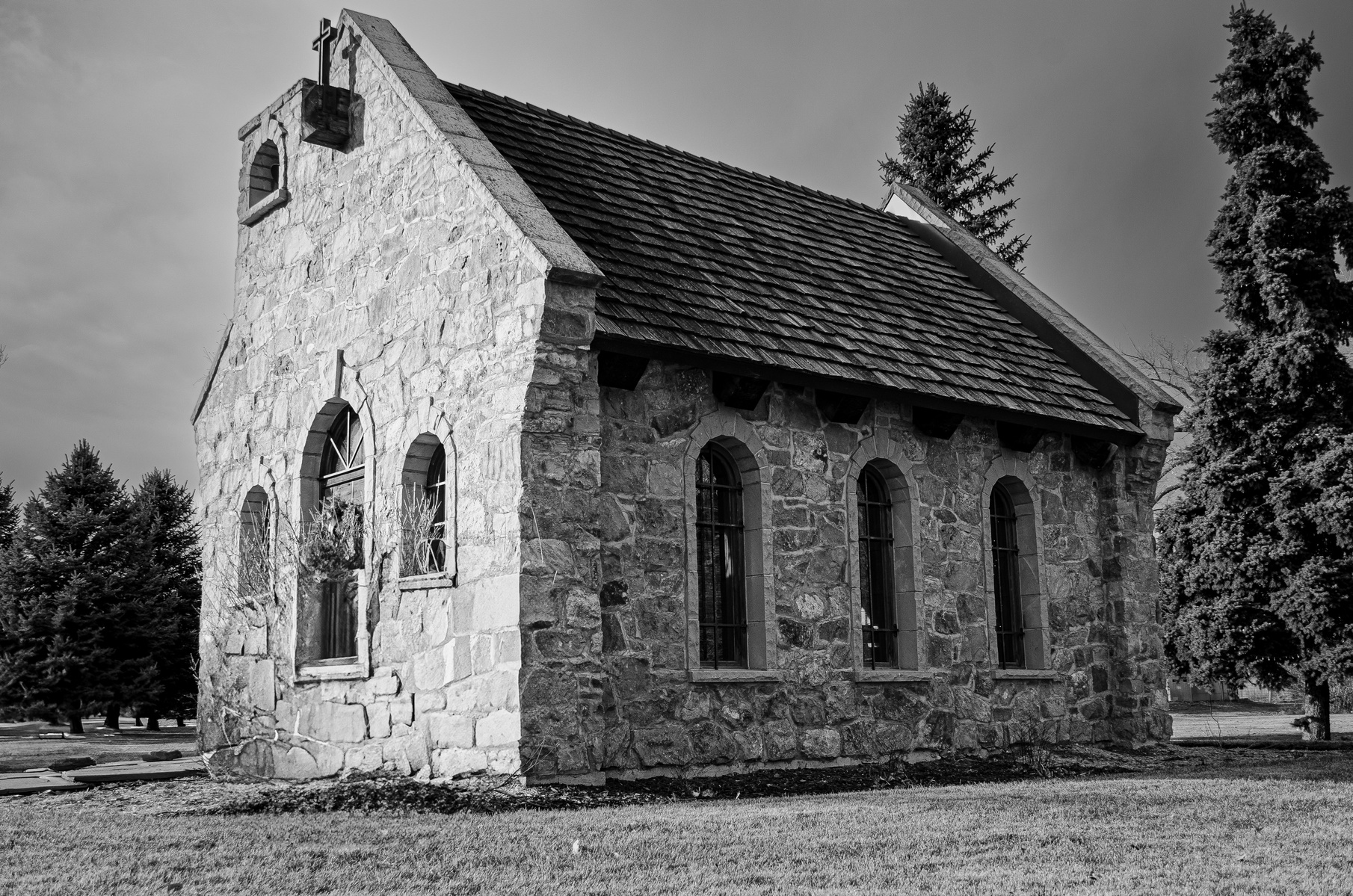 Small stone chapel with arched windows and shingled roof.
Tucked between trees and morning stillness, this chapel feels less like a building and more like a held breath—solid, quiet, and timeless.