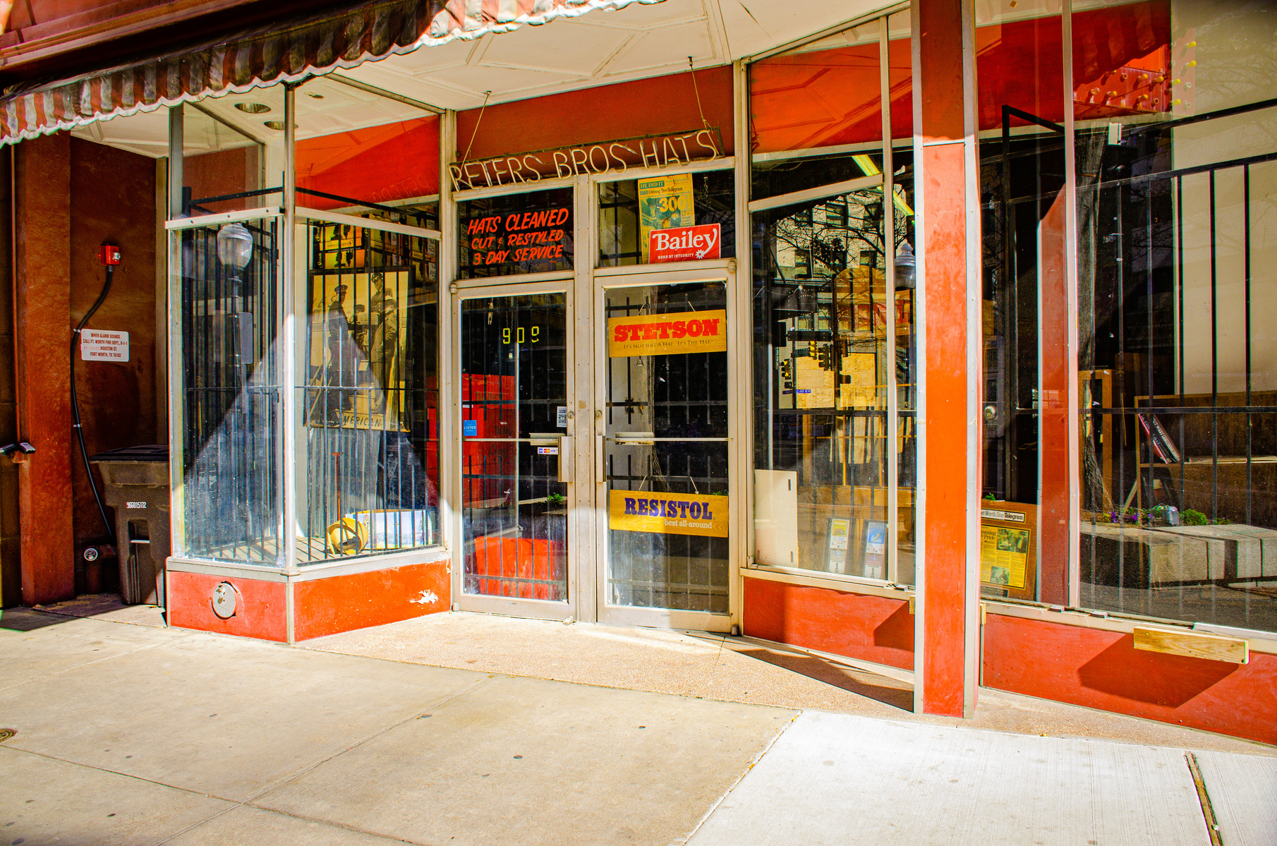 A storefront of display cases and Stetson signs. Inside, history still gets steamed and shaped—custom work for a changing world.