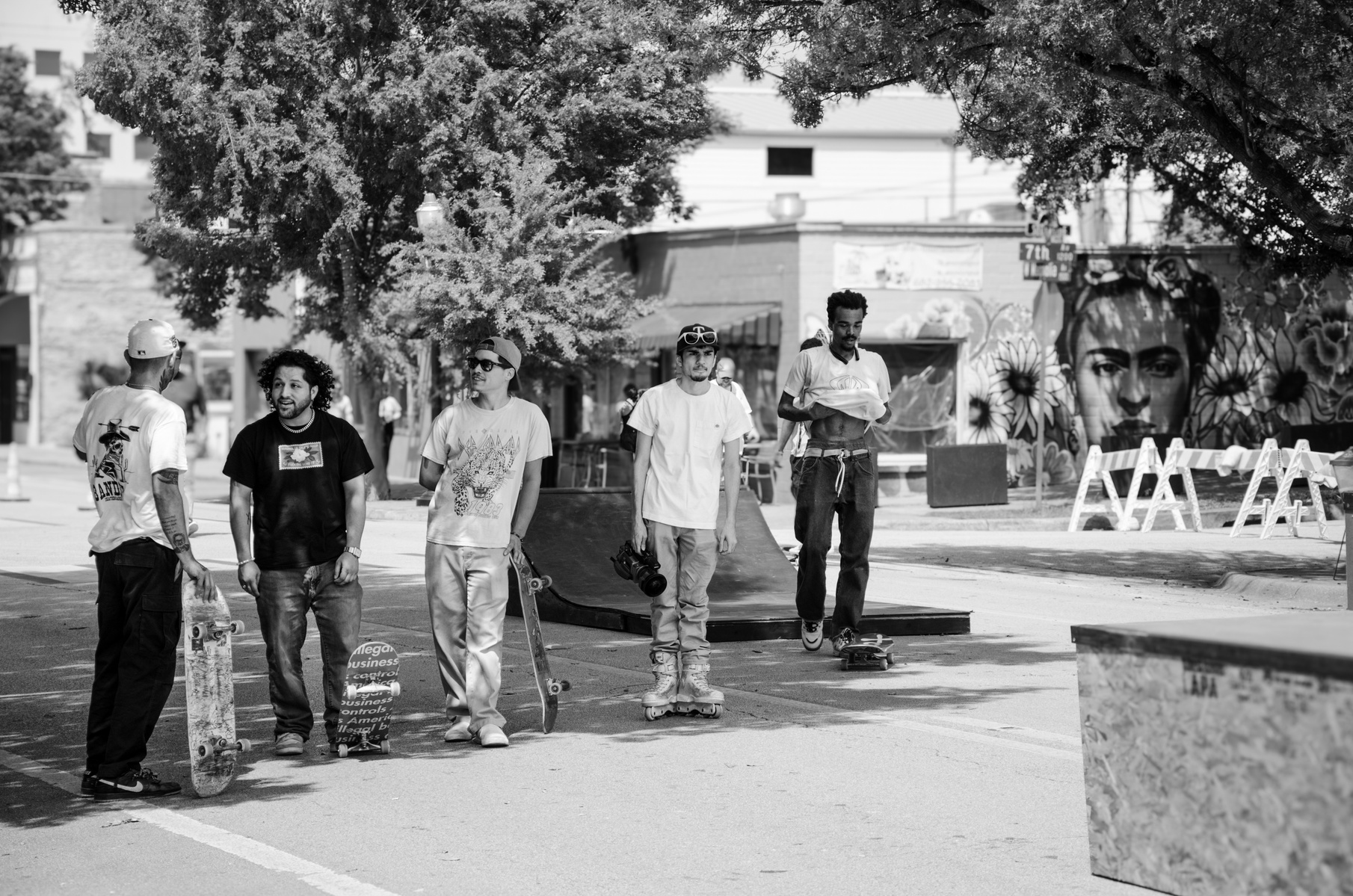 In the heat of day and rhythm of wheels, a loose circle of skaters bends the city to their tempo. Street becomes stage, gesture becomes language, and here—beneath the trees—they claim their fleeting dominion.