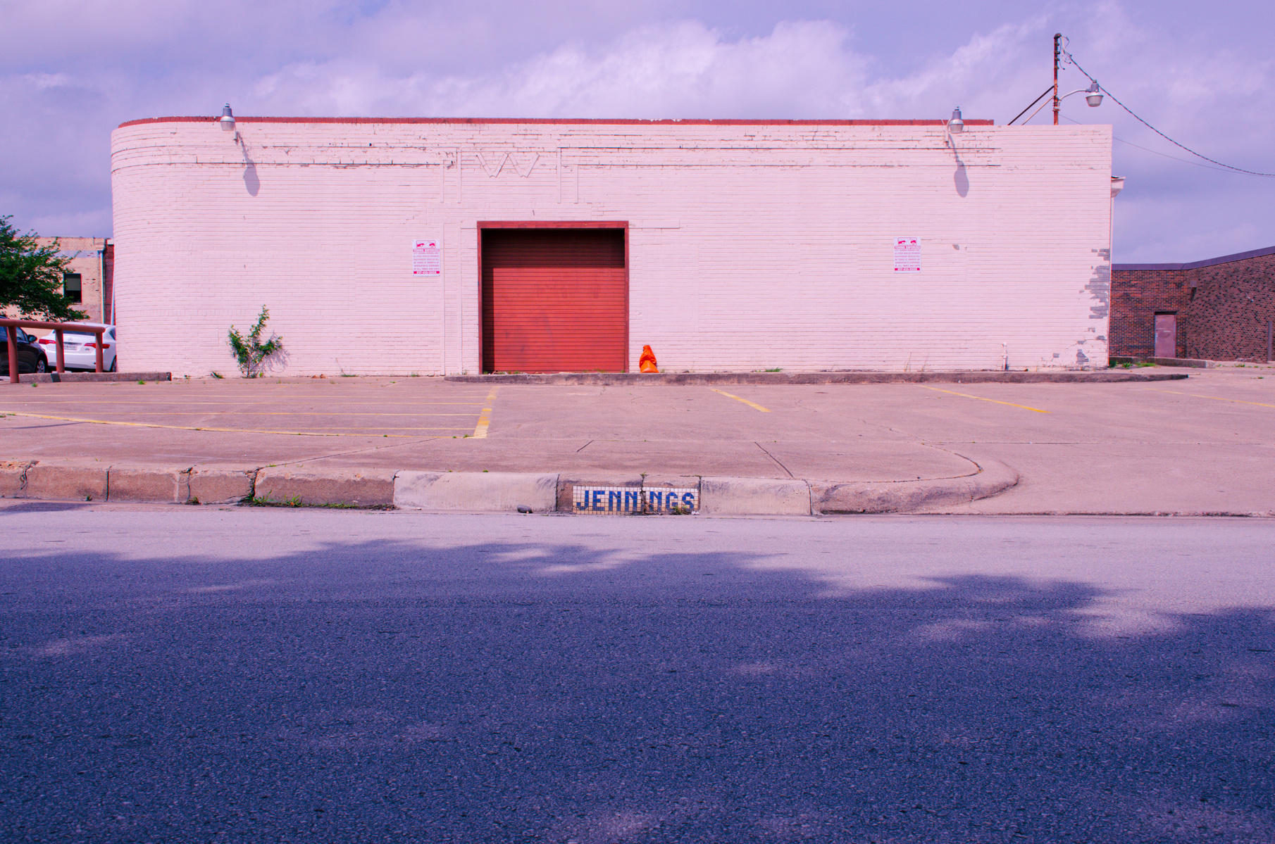 A pale facade, emptied of noise, stands like punctuation at the end of a long sentence. The painted wall holds the sun, a single cone left behind like a forgotten thought.