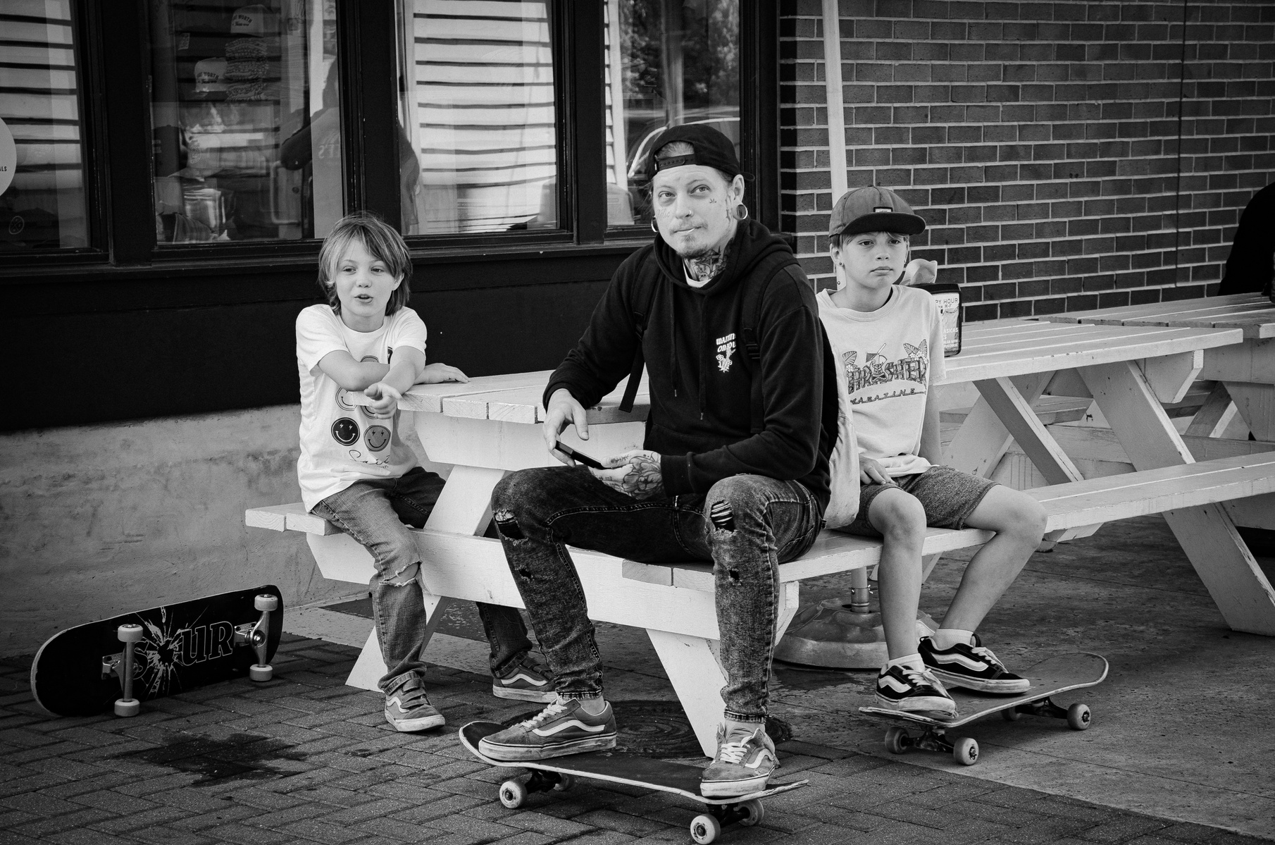 Youth clustered in thought, breath, and posture. A trio framed by concrete and waiting—the stillness before the grind, the camaraderie between bruises. Life rides beside them, unhurried.