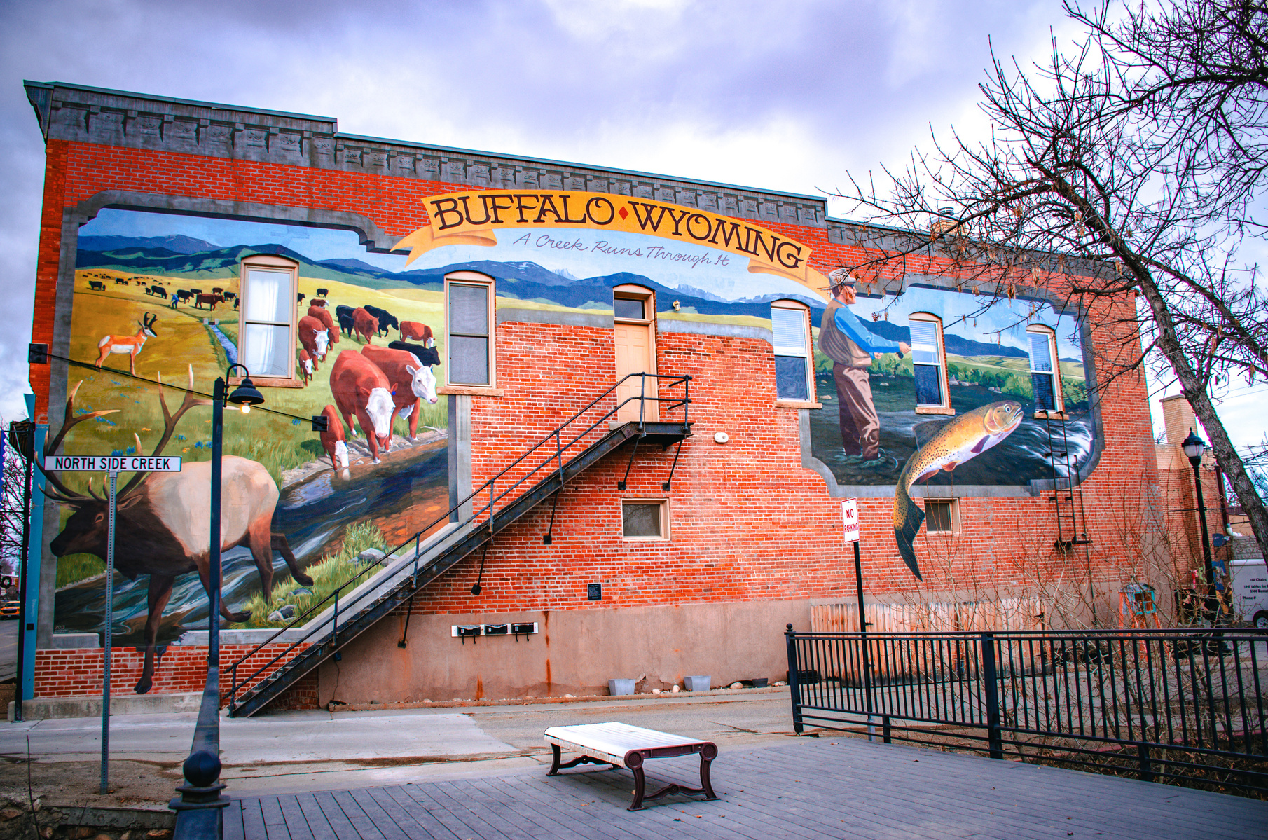 A mural within a mural. Life as layers, painted over time. The fish leaps from a memory we didn’t know we had. Somewhere between land and river, a man watches the past cast forward.