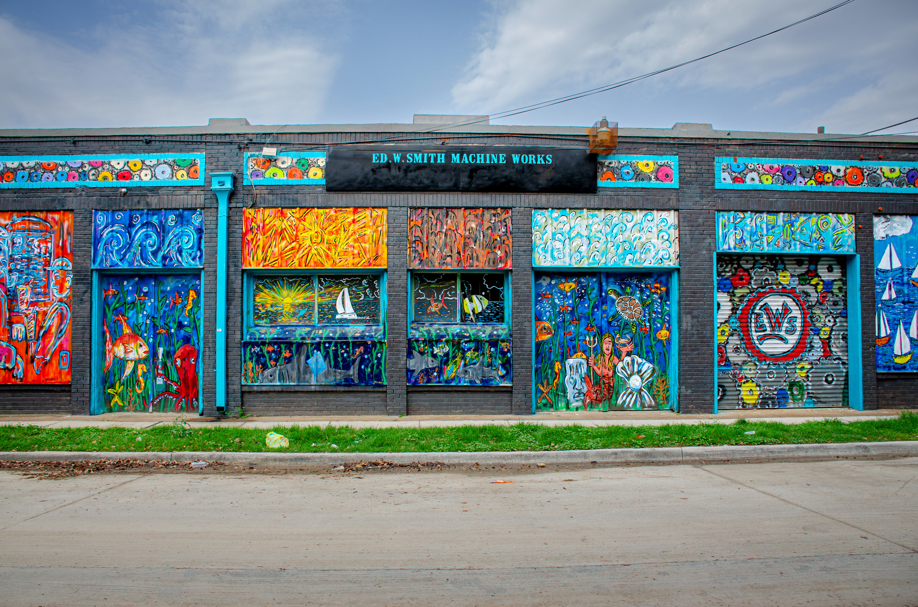 A once-industrial facade now radiates with underwater fantasies, sunbursts, and swirling currents. Each panel vibrates with its own story, transforming a utilitarian space into a kaleidoscope of color, curiosity, and movement.
