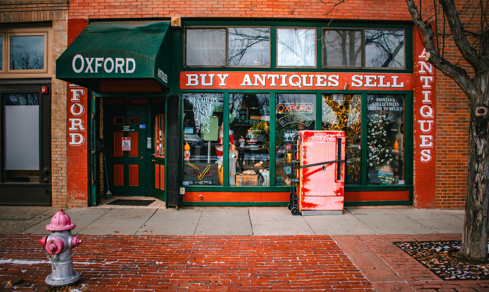 Oxford Antiques spills over with dusty records and forgotten knickknacks. A faded Coca-Cola machine stands sentry, red against red brick, like a relic refusing to rust away.